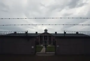 Exterior of a correctional facility with barbed wire under a cloudy sky